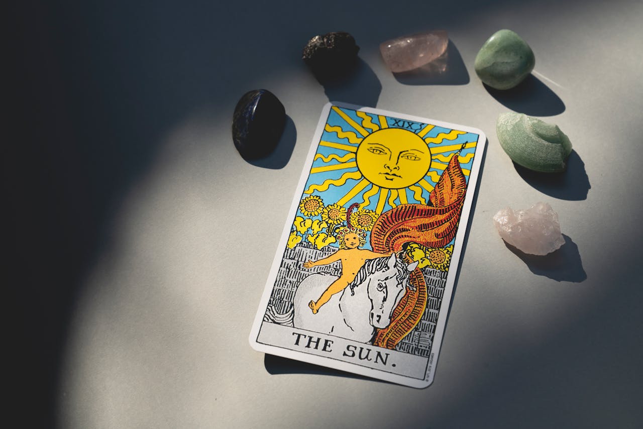 The Sun tarot card and crystals arranged on a surface with dramatic lighting and shadows.